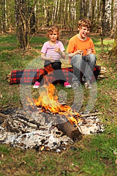 Two children sit near campfire