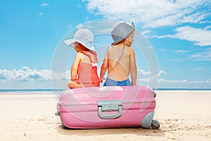 Two children sit on suitcase at the beach concept