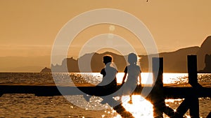 Two Children Sitting On Bridge At Sunset