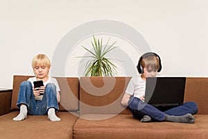 Two children sitting on couch with gadgets smartphone and laptop. Generation Alpha