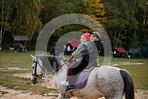 Two children are sitting on a horse, happy children are walking in the forest with a horse.