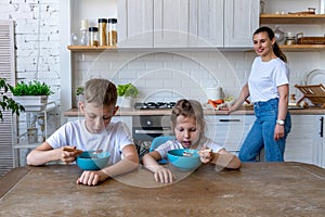 Two children are sitting table in the kitchen eating breakfast