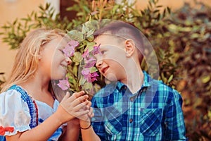 Two children smell the flowers green tree background. Boy brother gives a flower to the girl sister. Love care concept