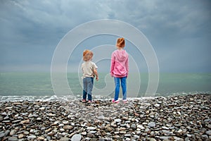 Two children stand on the seashore and look into the distance