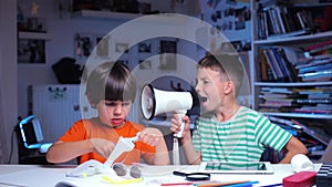 Two children at the table, one child screams, the second cuts out of paper