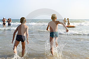 Two children on their backs running into the sea water