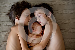 Two children, toddler and his big brother, hugging and kissing their newborn baby brother at home