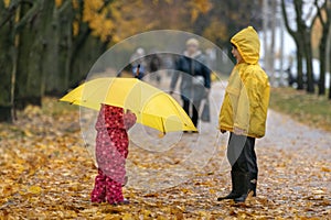 Two children are walking in the autumn park. Child under large yellow umbrella. Rainy day