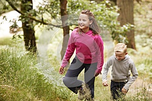 Two children walking through a forest amongst greenery, front view