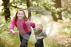 Two children walking in a forest amongst greenery smiling at camera, front view, focus on foreground