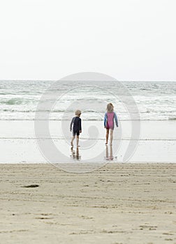 Two children, a young boy and a young girl, running through shallow waves and playing at the beach