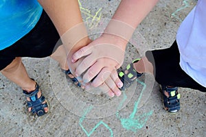 two childrens hands, drawing with chalk on the asphalt as a small child.