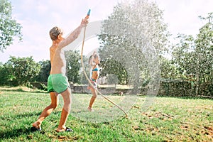 Two childs play together in garden, hot summer day, they make a raim from garden watering hose