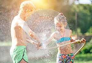 Two childs playing in garden, pours each other from the hose, makes a rain. Happy childhood concept image