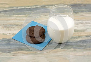 Two chocolate cookies with chocolate chips and glass of milk