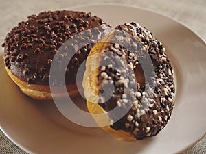 Two chocolate doughnut on a white plate and a cup of tea on a simple table cloth, Concept break, breakfast. Two taste chocolate