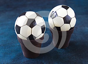 Two chocolate football balls cake in chocolate pots. A sweet gift for a child football fan on a beautiful blue table