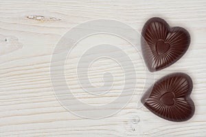 Two chocolate hearts on light wood background