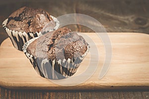 two chocolate muffins on a wooden tray and dark table/two chocolate muffins on a wooden tray and dark table. Selective focus