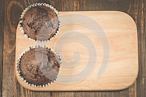 two chocolate muffins on a wooden tray and dark table/two chocolate muffins on a wooden tray and dark table. Top view and