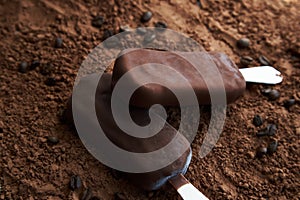 Two chocolate popsicles on a textured brown background made of cocoa powder and coffee beans