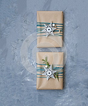 Two Christmas gifts in craft paper wrapped in blue thread with white snowflakes and rosemary branches on a gray concrete