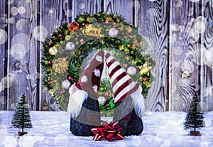 Two Christmas gnomes (elves) on the background of a Christmas wreath, red ribbon and artificial Christmas trees.