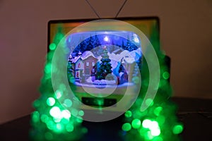 Two Christmas trees with light up bulbs around them around a tv with a snowy village