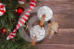 Two christmas white drink eggnog with marshmallow and cinnamon sticks and on woodn brown background with fir-tree