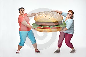 Two chubby women are holding a huge sandwich