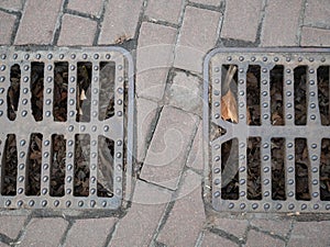 Two city sewer grids on a pavement for rain water flows to prevent flood