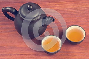 Two clay glazed tea bowls with brewed pu-erh tea and clay teapot on red wooden table vintage filtered