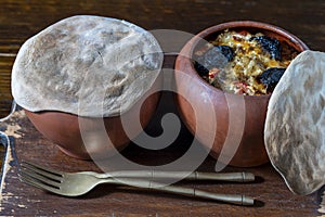 Two clay pots with stewed vegetables on a wooden table, closeup. Stewing food in earthenware is considered healthy