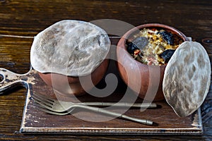 Two clay pots with stewed vegetables on a wooden table, closeup. Stewing food in earthenware is considered healthy