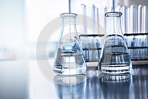 Two clear flask with water in front of test tube in education chemistry science laboratory background