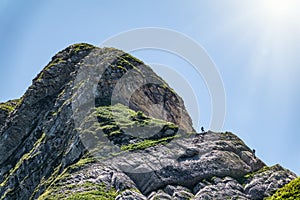 Two climbers climb a high rock on a background of blue sky and sun