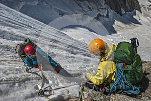 Two climbers on a steep snow-ice slope on insurance. Cracked glacier