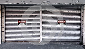 Two closed corrugated metallic Roll up doors with closed permanently signs. Concept of closed, shuttered or bankrupt establishment