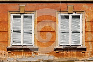 Two closed dilapidated windows with white wooden frames and broken plastic window blinds mounted on wall of old suburban family