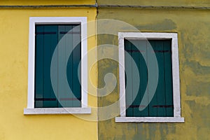 Two closed green windows on a yellow wall