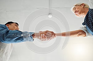 Two clothing designers shaking hands while working together at a shop. Mature caucasian woman and young asian man giving