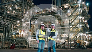 Two co-workers are talking at the oil-processing factory at night