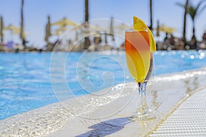 Two cocktails with natural juice and ice at the edge of the swimming pool. Orange cocktail with an orange slice and red