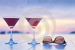 Two cocktails and sunglasses on a table of luxurious tropical beach resort restaurant with beautiful sunset in the background