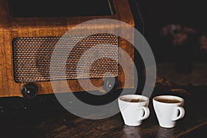 Two coffee cups with espresso and retro radio on dark wooden background. Vintage color tone