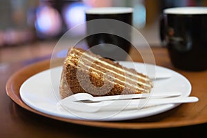 Two Coffee cups, plate with carrot cake or pie, disposable plastic knife, fork and spoon on a round tray on a table in a