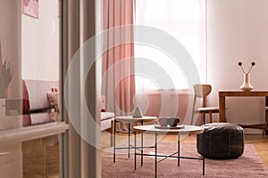 Two coffee cups on wooden coffee table in chic pastel pink living room with oldschool leather pouf on warm pastel pink carpet