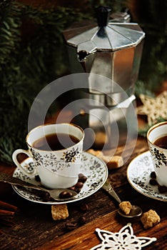 Two cups of espresso with pieces of cane sugar and Italian coffee maker on wooden table.