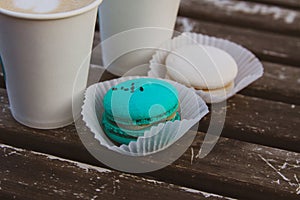 Two coffee in paper cups, two macaroons of mint and white color on a wooden vintage table.