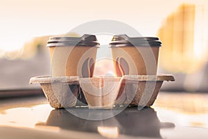 Two coffee paper glasses look at each other in the sunshine on a blurred city background. Love concept